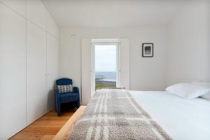 a white bedroom with a bed and a blue chair at João de Oliveira casas de campo in Santo António +148 photos