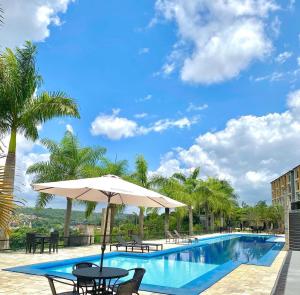 a swimming pool with an umbrella and tables and chairs at Apartamento de um quarto com varanda externa in Bananeiras
