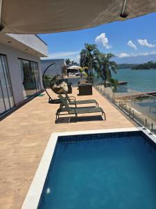 a house with a swimming pool next to the water at Maravilhosa casa linear 5 suítes em Angra in Angra dos Reis