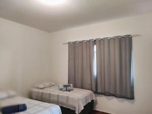 a room with two beds and a window with curtains at Quarto privativo no Bairro Santa Mônica in Uberlândia