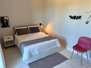 Un dormitorio con una cama y una silla rosa. en Bertholi Beira-Mar, en Serra