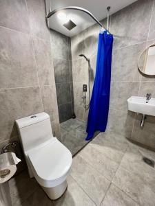 a bathroom with a toilet and a shower with a blue shower curtain at Queensland Suites at Aru Suites, Kota Kinabalu 2 Bedroom Family Suite in Kota Kinabalu