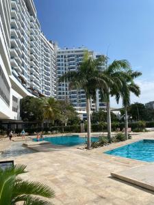 a swimming pool with palm trees and a large building at Condominio Reserva del mar Santa Marta in Gaira