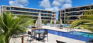 a resort with a pool and a table and chairs and a building at Porto de Galinhas - Muro Alto, Malia Beach Experience in Ipojuca