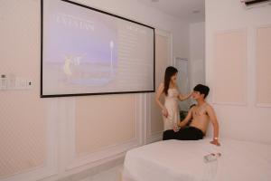 Un uomo e una donna seduti su un letto di fronte a uno schermo di Đào Hoa Homestay a Quy Nhon