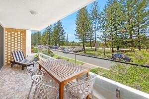 a balcony with a wooden table and chairs and a view of a street at Beachfront Retreat at Burleigh, Breezy and Cosy in Gold Coast