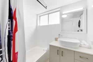 a white bathroom with a white sink and a tub at Beachfront Retreat at Burleigh, Breezy and Cosy in Gold Coast +17 photos