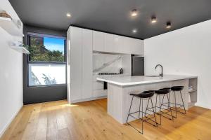 una cucina con armadi bianchi e bancone con sgabelli da bar di Stylish Three-Story Getaway with Balcony - Clayton a Clayton North