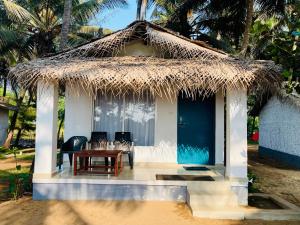 戈卡尔纳The Meraki Beach Resort Gokarna的一个带稻草屋顶和桌椅的小小屋