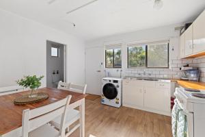 a kitchen with white cabinets and a wooden table and a dining room at Little Pier Cottage in Inverloch +13 photos