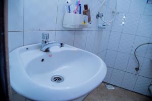 a white sink in a white tiled bathroom at Cozy Studio Apartment Makindye in Kampala +2 photos