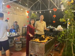a man and woman standing next to a grill with food at Homestay Nhà Mộc in Da Lat