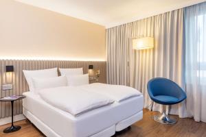 a bedroom with a white bed and a blue chair at NH Hamburg Altona in Hamburg