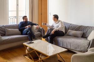 two men sitting in a living room playing a video game at Ômarais Guest House in Paris