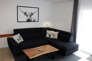 Ferienhaus Nr 93, Kategorie Komfort Plus, Feriendorf Hochbergle, Allgäu في Karlsebene: غرفة معيشة مع أريكة سوداء وطاولة +11 صورة