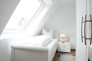 a white bedroom with a white bed and a window at Deichnähe - D in Norden