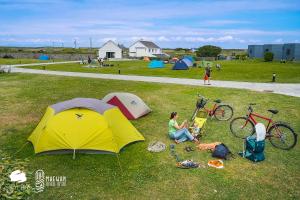 a woman sitting in the grass next to a tent at Aran Islands Camping & Glamping in Kilronan