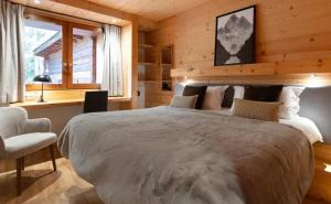 Chalet Les Arolles- Catered Chalet -Half Board في تينيِ: غرفة نوم بها سرير كبير وكرسي