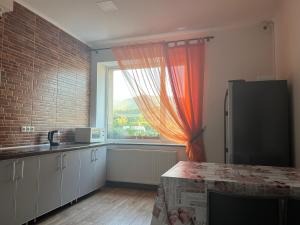 eine Küche mit einem großen Fenster und einem orangefarbenen Vorhang in der Unterkunft PETROVICH hotel in Chust