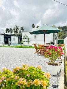 a patio with a table and an umbrella and flowers at Tiny House Merchang, Marang Roomstay Homestay in Kampong Pulau Rusa Baru