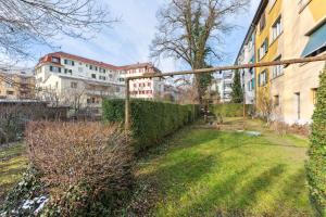 einem Garten mit Hecke und Gebäuden im Hintergrund in der Unterkunft Basic Apartment with Full Kitchen in Zürich