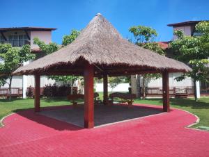 a pavilion with a straw umbrella and benches on a red carpet at Flat Club meridional B3 1ps in Tamandaré