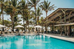 a swimming pool with chairs and umbrellas and palm trees at Crystals Beach Resort Belle Mare, a member of Radisson Individuals in Belle Mare