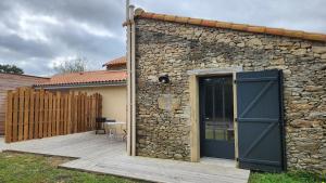 a stone building with a door and a wooden deck at Studio 2-3 pers in La Gaubretière