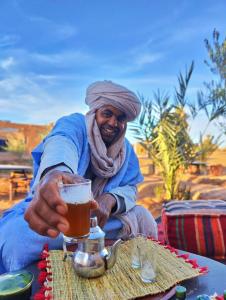 Un uomo che tiene un bicchiere di birra su un tavolo di Nomads Heaven Camp a M'Hamid