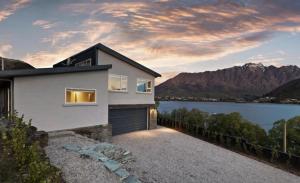 a house with a garage next to a body of water at Mountain View Paradise 3 Bedroom House Lake Views in Queenstown