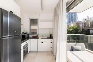 a kitchen with white cabinets and a stainless steel refrigerator at The Shoreline By Localz - Beach Complex in Tel Aviv +145 photos