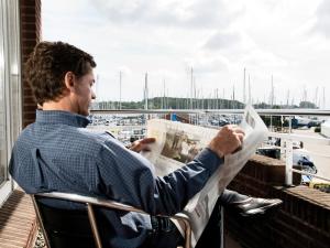 un homme assis sur une chaise lisant un journal dans l'établissement ancora Marina Haus 2 Nr 02, Typ 2, à Neustadt in Holstein