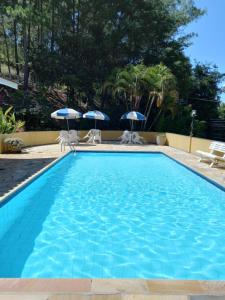 a swimming pool with two chairs and umbrellas at Casa Charmosa e Aconchegante em Serra Negra - SP in Serra Negra