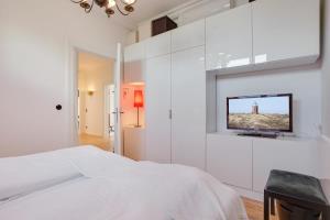 a white bedroom with a bed and a tv on a wall at Die Schlosserei in Westerland