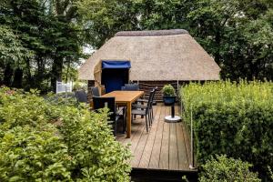 eine Holzterrasse mit einem Tisch und einem Strohdach in der Unterkunft Ferienhaus Katzhörn in Emmelsbüll-Horsbüll
