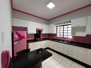 a large kitchen with white cabinets and pink walls at Colibri Inhouse Santa Cruz in Rondonópolis