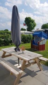 Una mesa de picnic de madera con una sombrilla grande encima. en Campingland Ostsee - Mobilheim 61Meeresstille, en Schashagen