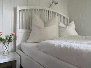 een wit bed met witte kussens en een vaas met bloemen bij Ferienwohnung Harz #3, Pool, Sauna, WLAN in Hohegeiß
