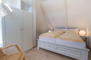 a white bedroom with a bed and a chair at Abaco 4N in Wenningstedt