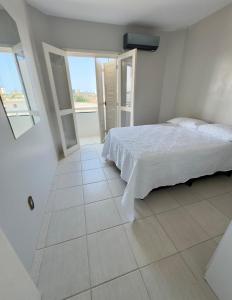 a white bedroom with a bed and a window at Cobertura duplex 3 quartos, centro, terraço e churrasqueira, ideal para família, acesso por escadas in Torres +9 photos