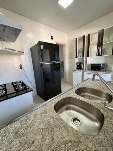 a kitchen with a sink and a black refrigerator at Cobertura duplex 3 quartos, centro, terraço e churrasqueira, ideal para família, acesso por escadas in Torres