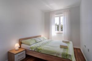 a white bedroom with a bed and a window at Apartment Mirna in Nerezine