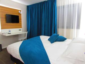 a bedroom with a bed with blue curtains and a tv at Brit Hotel & Spa Saint Brieuc Plérin in Plérin