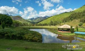 a gazebo next to a lake with mountains at Hotel Fazenda Jecava in Campanha