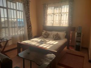 a bedroom with a bed and a table and windows at Kimberly's Guesthouse in Munyu