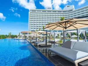 a hotel swimming pool with lounge chairs and umbrellas at Grand Mercure Okinawa Cape Zanpa Resort in Yomitan