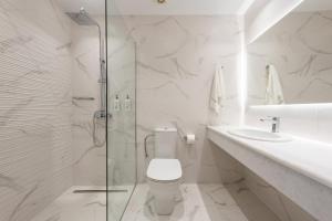 a white bathroom with a shower and a toilet and a sink at Saint George Hotel in Chrissi Akti