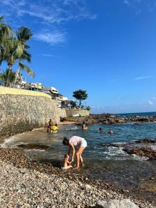 a woman and a child playing on a rocky beach at Casa Circuito Carnaval frente à praia in Salvador