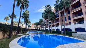 a swimming pool in front of a building with palm trees at Vilamar VyB in Denia