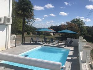 a pool with chairs and umbrellas next to a house at Condrine in Doazit